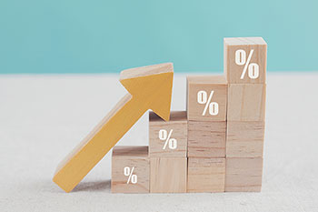 Bloccheti di legno messi a scala, su alcuni è disegnato il simbolo della percentuale in bianco. Sui blocchetti poggia una freccia verso l'alto, gialla.