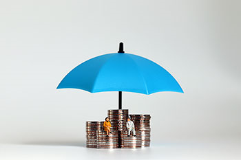 Due persone sedute su pile di monetine coperte da un ombrello blu.