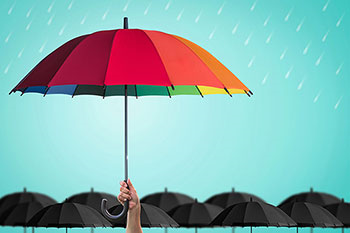 una mano solleva in alto un ombrello dai colori dell'arcobaleno e sullo sfondo tanti ombrelli neri