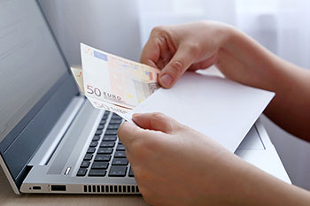 mani femminili tengono una busta con dei soldi, davanti ad un pc portatile