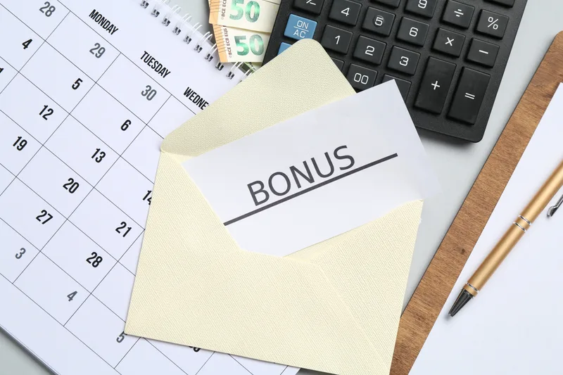 biglietto con la scritta bonus, calendario, calcolatrice, banconote e una penna