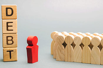 omini di legno grezzo in gruppo di fronte ad un omino di legno rosso e una torretta di cubetti di legno che formano la scritta 'debt'