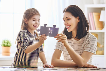 Mamma e figlia che, nel confort domestico, accostano fra loro due tessere di un puzzle.