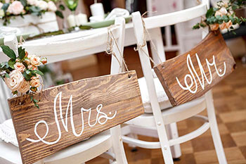 Sedie bianche per la sposa e lo sposo al ricevimento di nozze con le targhette Mrs e Mr in legno appese allo schienale