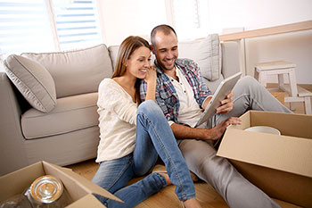 coppia che guarda il tablet seduta sul pavimento davanti al divano con attorno degli scatoloni